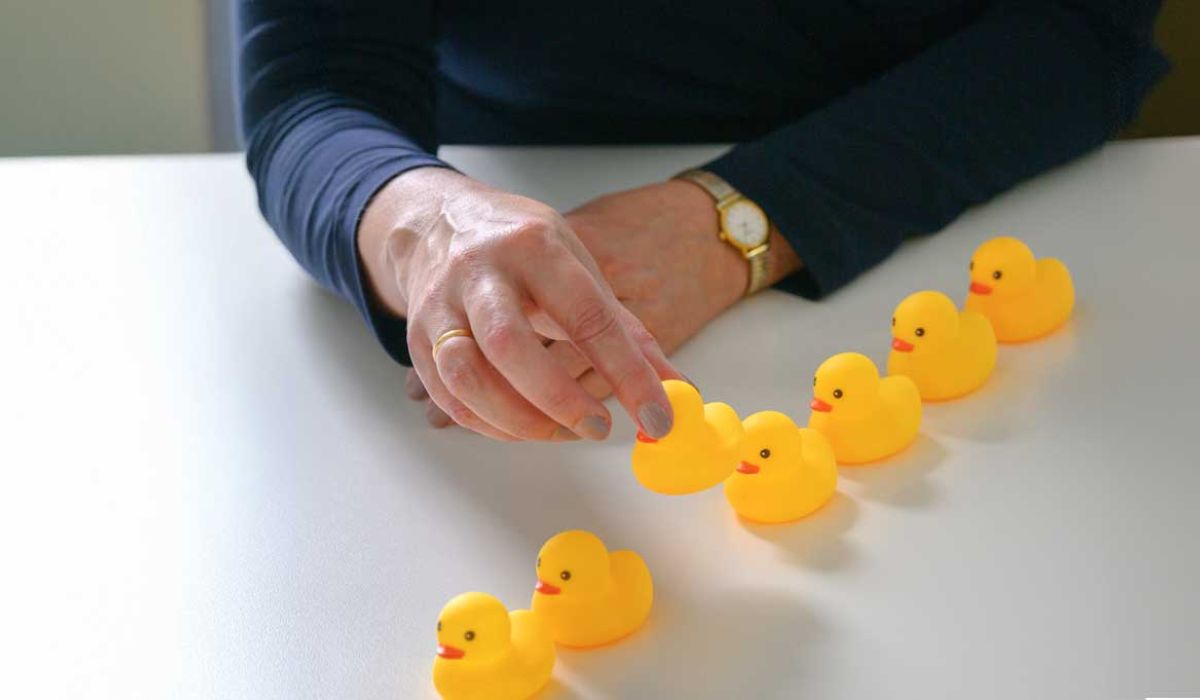 A woman carefully arranges colorful rubber ducks in a neat row on a flat surface.