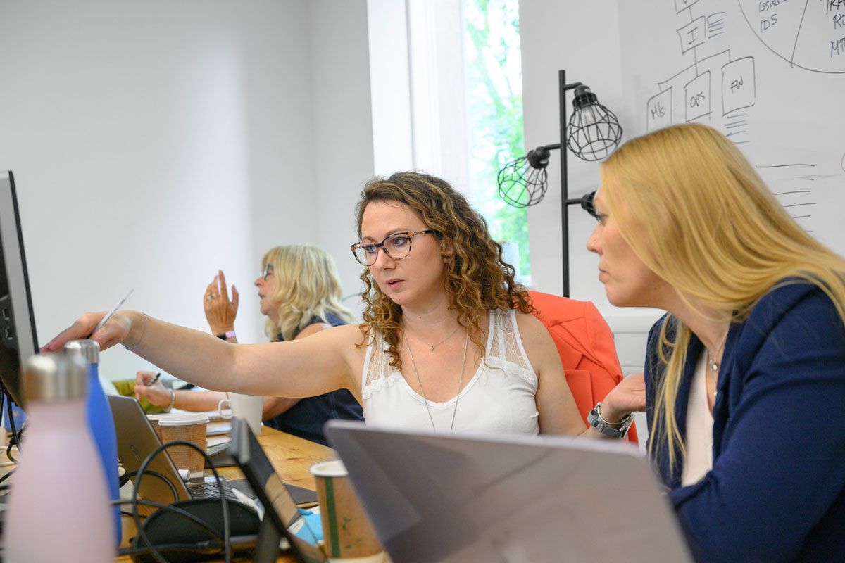 A woman points at a computer screen while two other women observe attentively.